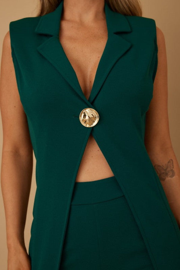 Green sleeveless blazer with a gold button on a beige background